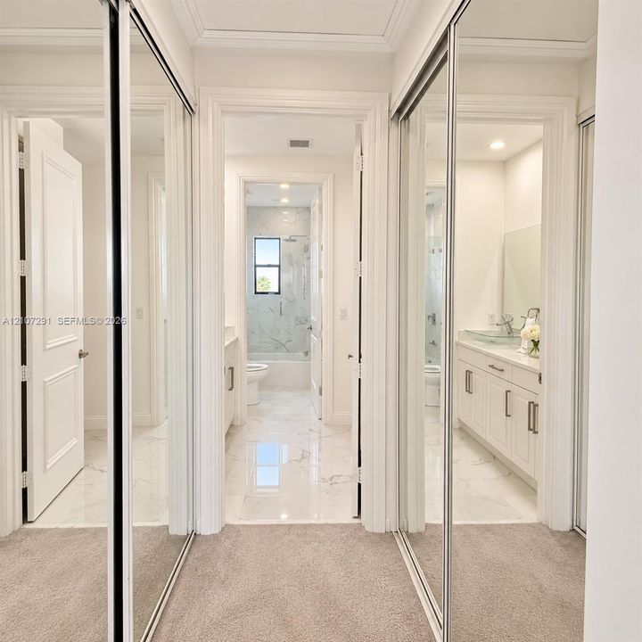 Floor-to-ceiling mirrored closet doors, white cabinetry with brushed-nickel hardware, stone-finish tile flooring, and integrated recessed lighting