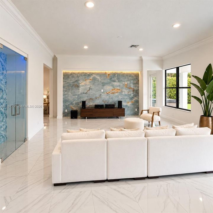 Large-format polished tile flooring, full-height stone feature wall with integrated accent lighting, recessed ceiling lighting, and large windows with black frames
