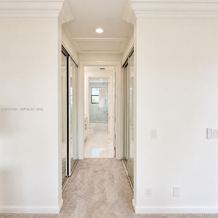 Hallway featuring dual mirrored-panel sliding closets, crown molding, neutral carpeting, and recessed lighting