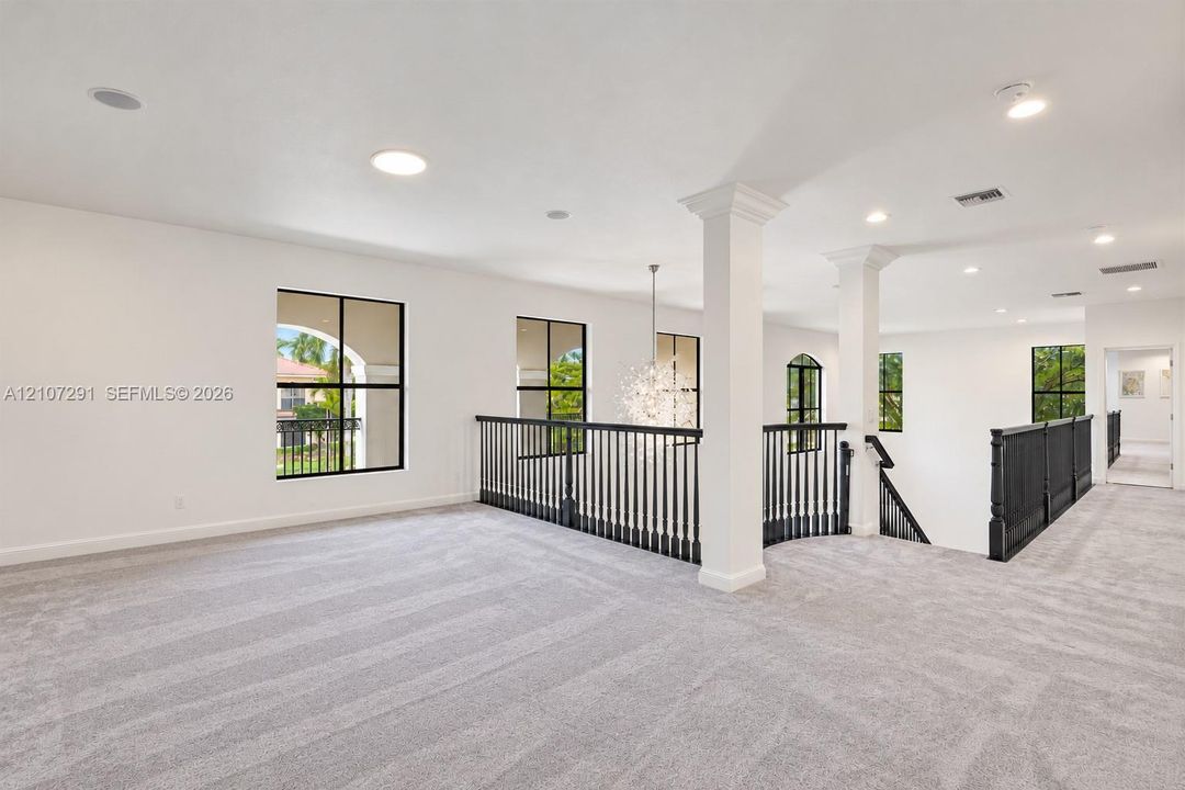 Open-concept area featuring neutral carpeting, recessed lighting, structural support columns, and black metal railings