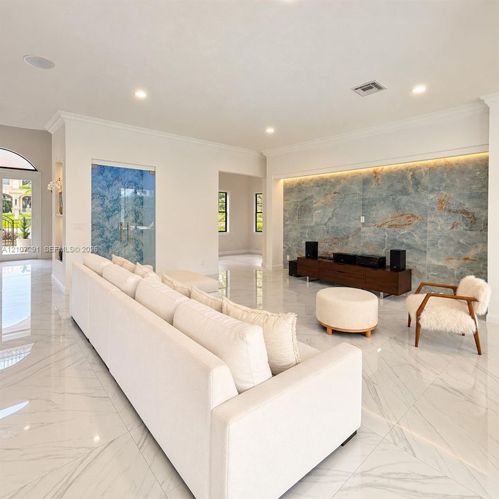 Open-concept interior featuring large-format polished stone flooring, a dramatic full-height natural stone accent wall with integrated ambient lighting, recessed ceiling lights, and arched glass entryway doors