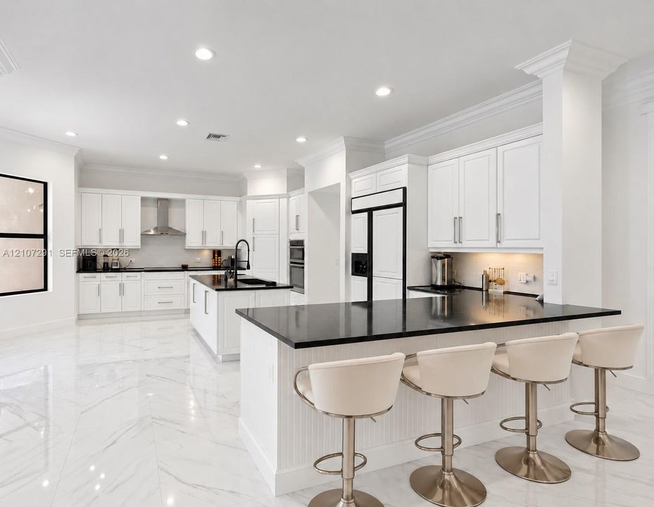 Kitchen featuring custom white shaker-style cabinetry, dark stone countertops, a large center island, recessed lighting, and large-format tile flooring