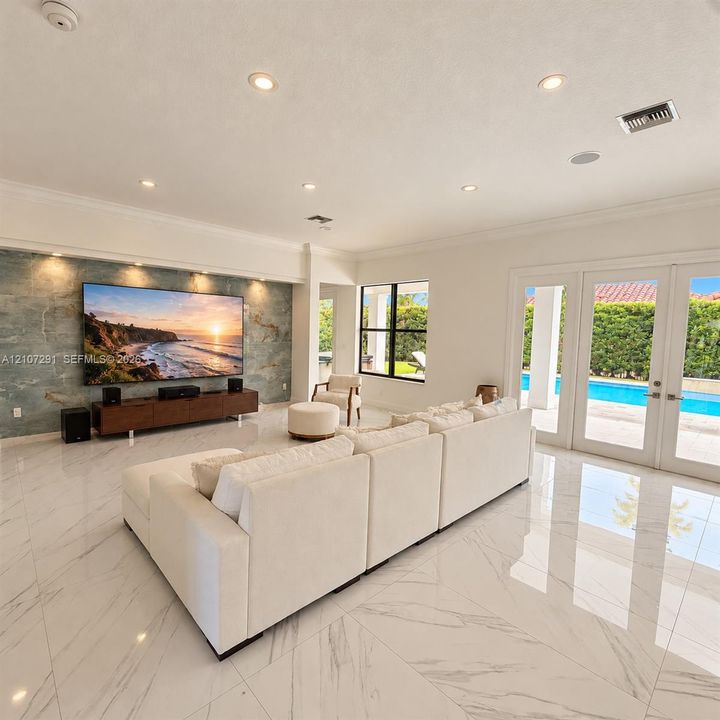 Living area featuring polished tile flooring, a stone-accented media wall with recessed lighting, and glass-paned double doors opening to a pool area