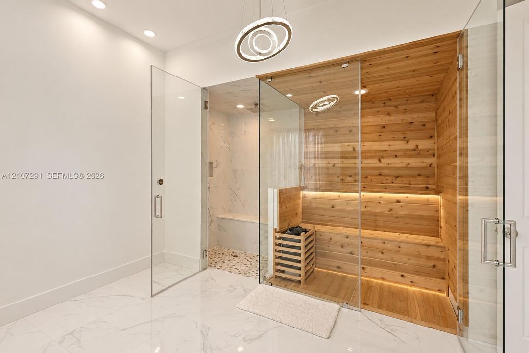 Custom sauna featuring wood-panelled interior, recessed lighting, and glass enclosure, paired with a glass-enclosed walk-in shower containing stone tile flooring, built-in bench seating, and polished finish floor tiles