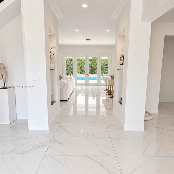 Polished stone flooring, dual recessed wall niches with glass shelving, crown molding, recessed lighting, and multi-pane glass french doors