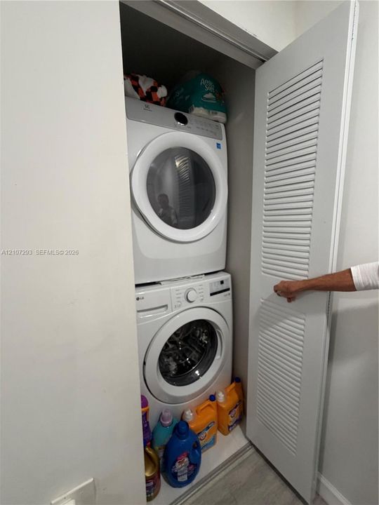 Stackable laundry closet featuring a white louvered door and wood-finish flooring