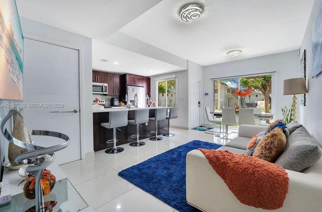 Open-concept living space featuring high-gloss tile flooring, espresso-toned cabinetry, a stone-surfaced breakfast bar, and sliding glass doors