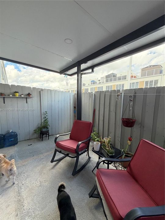 Covered patio featuring concrete flooring, a structural support post, a wall-mounted shelving unit, and privacy fencing