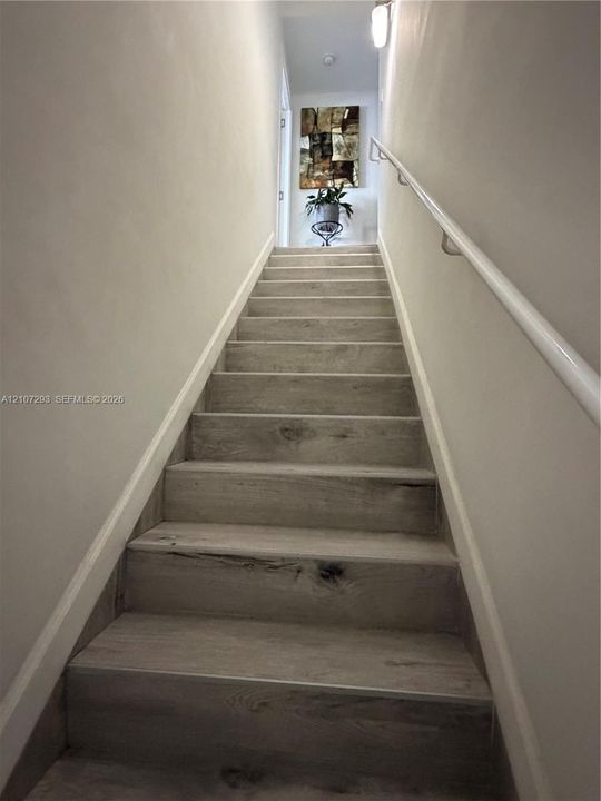 Staircase featuring wood-finish flooring treads and a white wall-mounted handrail