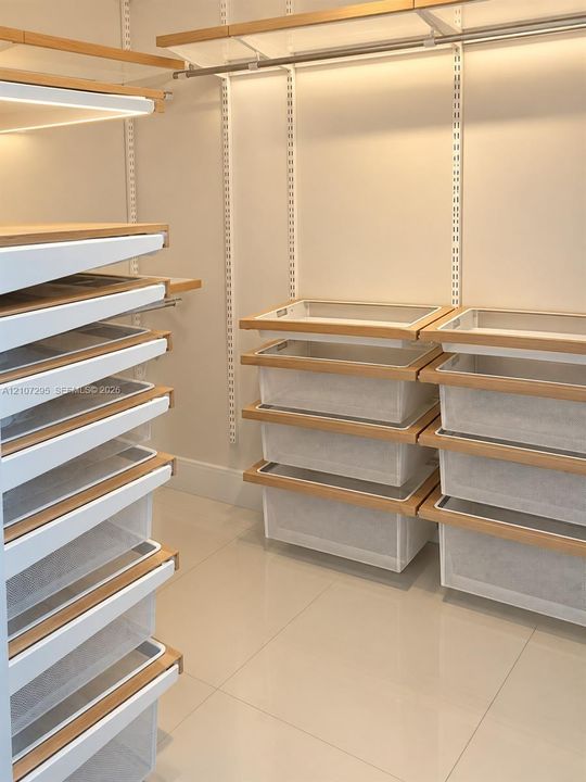 Custom closet system featuring adjustable shelving, integrated wire storage drawers, wood-finish trim, and polished tile flooring