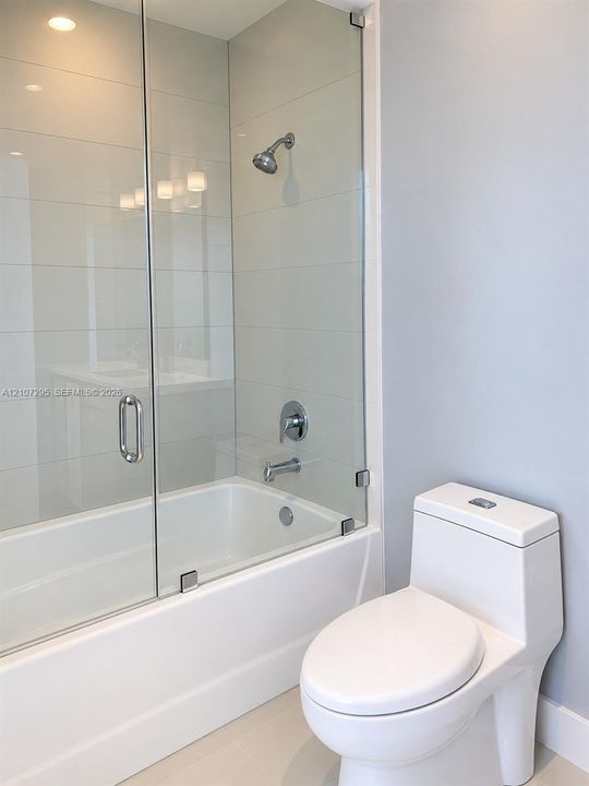 Bathroom featuring a tub-shower combination with floor-to-ceiling tile surround, a frameless glass door, chrome fixtures, and a dual-flush toilet