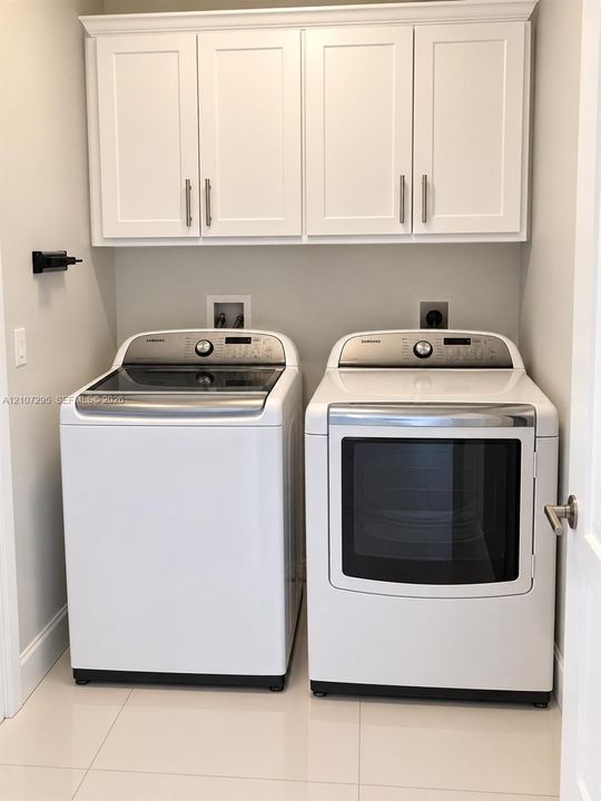 Laundry area featuring white shaker-style wall cabinetry with brushed nickel pulls and large-format tile flooring