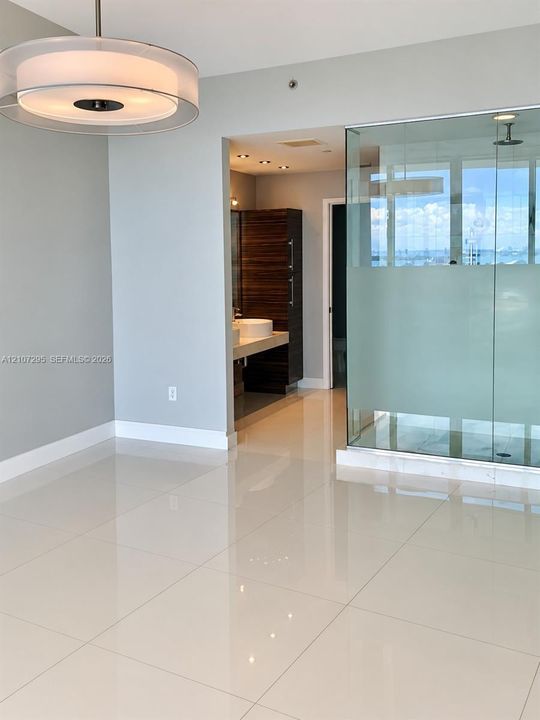 Large-format polished tile flooring, glass-enclosed shower with frosted privacy panel, circular contemporary drum pendant lighting, and vanity with integrated vessel sink and wood-finish cabinetry
