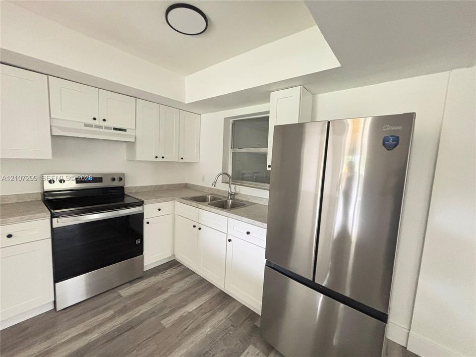 Kitchen featuring white shaker-style cabinetry, wood-finish flooring, stainless steel French-door refrigerator, matching electric range, and dual-basin sink with a goose-neck faucet