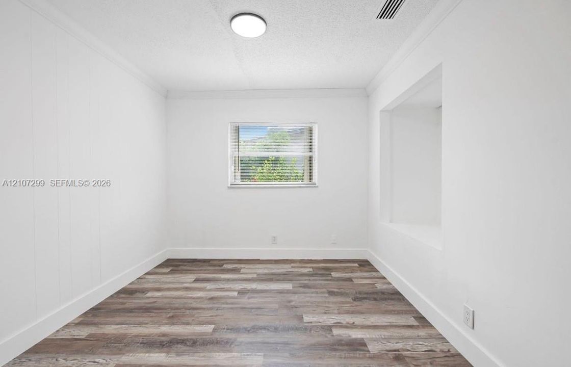 Interior space featuring wood-finish flooring, white walls, crown molding, a built-in wall niche, and a single window