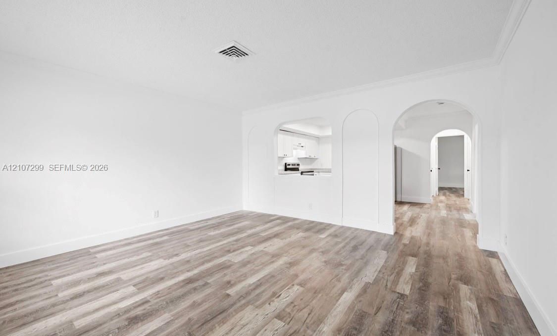 Interior space featuring wood-finish flooring, crisp white wall finishes, crown molding, arched architectural detailing, and a passthrough window