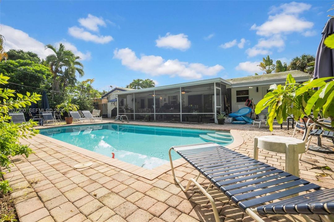 In-ground pool featuring built-in stairs, enclosed screen lanai, and expansive paver patio