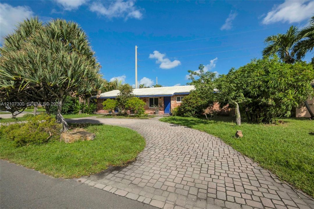 Single-story brick exterior featuring a curved paver driveway, mature landscaping, and an expansive lawn