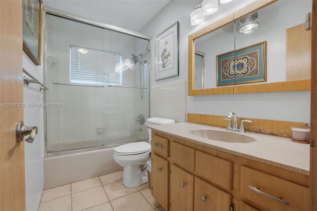 Bathroom featuring wood cabinetry, a light-toned solid surface countertop with an integrated basin, a combination bathtub and shower with glass sliding doors, and a built-in medicine cabinet with integrated lighting