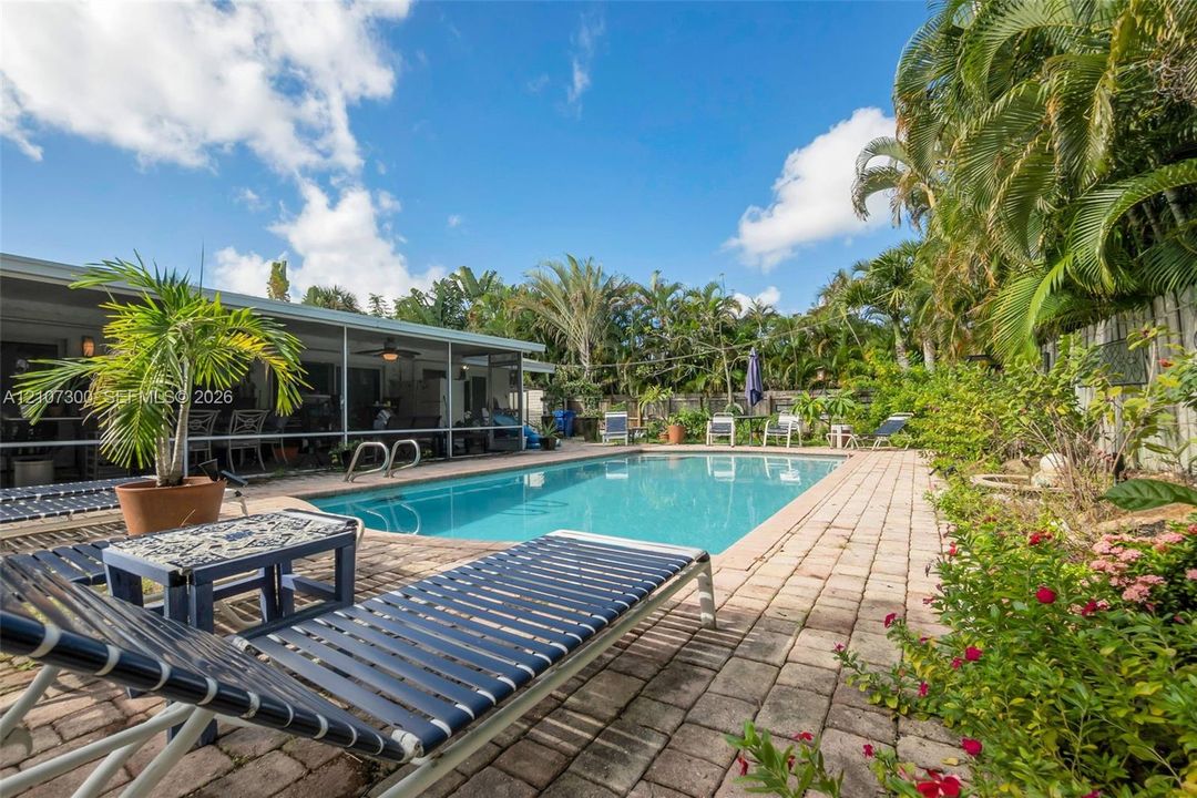 Outdoor swimming pool with brick paver decking, screened-in lanai, and mature perimeter landscaping