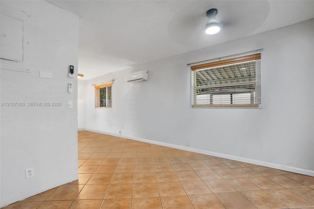 Neutral-toned interior space featuring ceramic tile flooring, wall-mounted ductless air conditioning unit, ceiling-mounted lighting, and horizontal window blinds