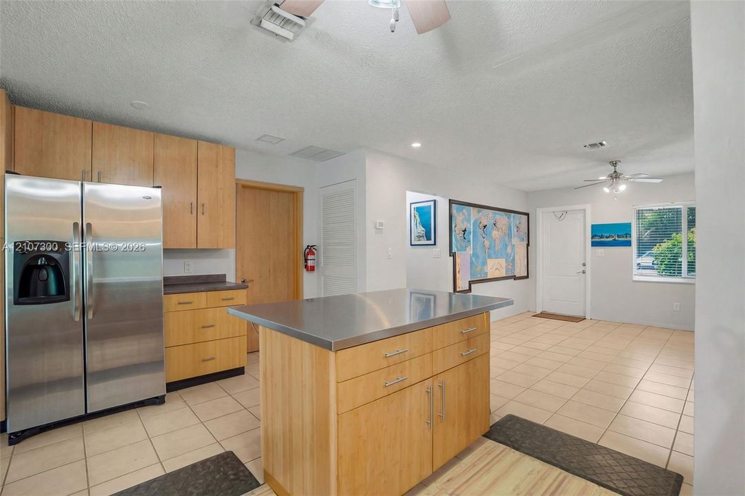 Kitchen featuring wood cabinetry, stainless steel refrigerator, stainless steel island countertop, and tiled flooring