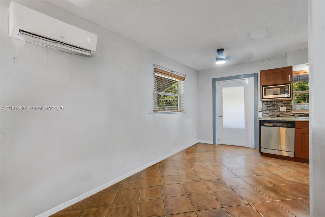Wall-mounted ductless air conditioning unit, tile flooring, window with blinds, full-lite exterior door, and built-in kitchen cabinetry with stainless steel appliance
