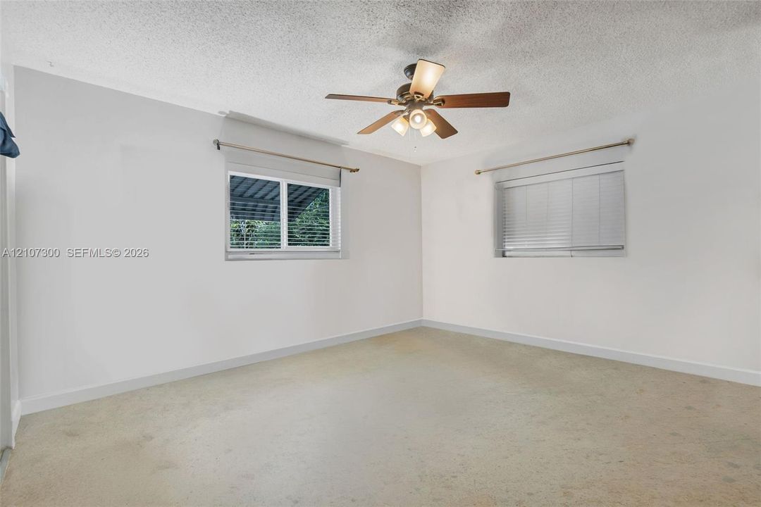 Interior room featuring neutral wall finishes, carpeted flooring, two windows with horizontal blinds, and a ceiling fan with integrated lighting