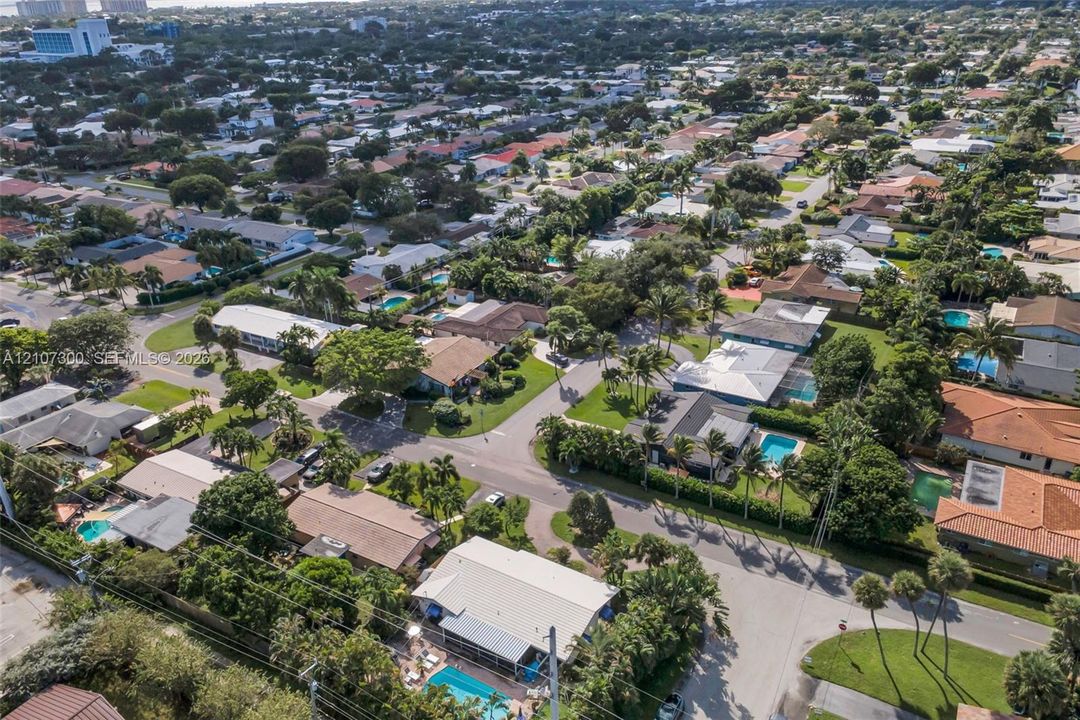 Aerial perspective of a suburban neighborhood featuring residential lots with mature trees, paved streets, and private swimming pools