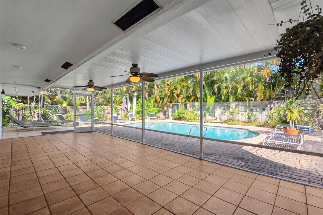 Screened-in lanai featuring tiled flooring, recessed ceiling lighting, and overhead paddle fans, opening to a swimming pool with a paver patio