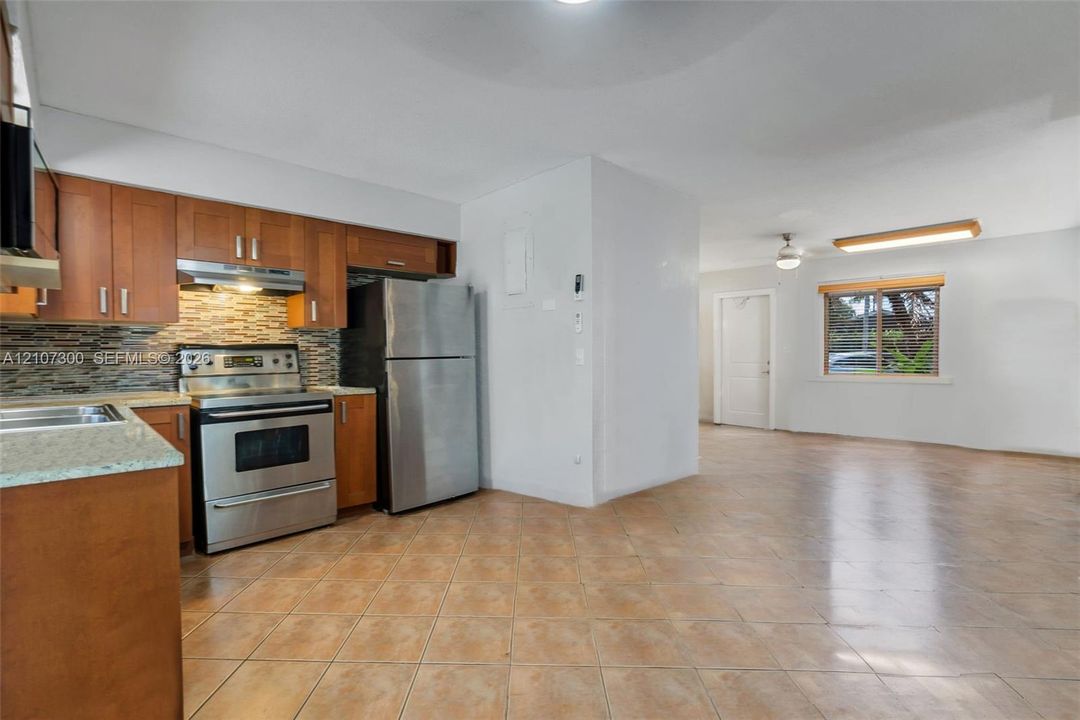 Kitchen featuring natural wood cabinetry, stone-texture backsplash, stone-surface countertops, stainless steel appliances, and ceramic tile flooring