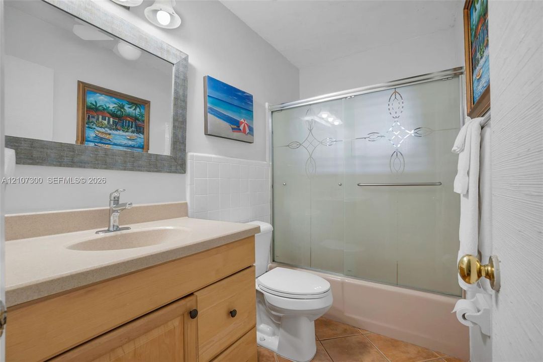 Bathroom featuring a natural wood vanity with a solid-surface countertop, an integrated sink, a framed wall mirror, and a tub-shower combination with sliding frosted glass doors