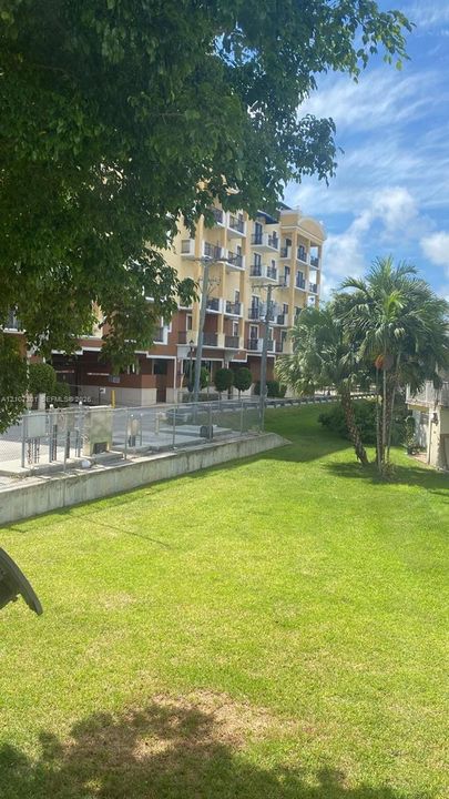 Multi-story exterior building featuring balconies with railings, concrete foundation, metal fencing, and landscaped grounds with mature trees