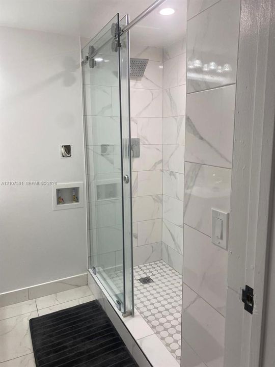 Walk-in shower featuring a frameless glass sliding door, large-format tile wall surround, recessed shower niche, rain-style shower head, and mosaic tile flooring