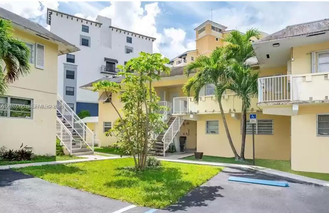 Multi-level exterior featuring light-toned stucco siding, open-air metal staircases, elevated private balconies with metal railings, and a landscaped courtyard