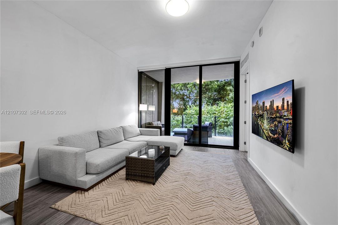 Living area featuring wood-finish flooring, floor-to-ceiling sliding glass doors, and a glass-railed balcony