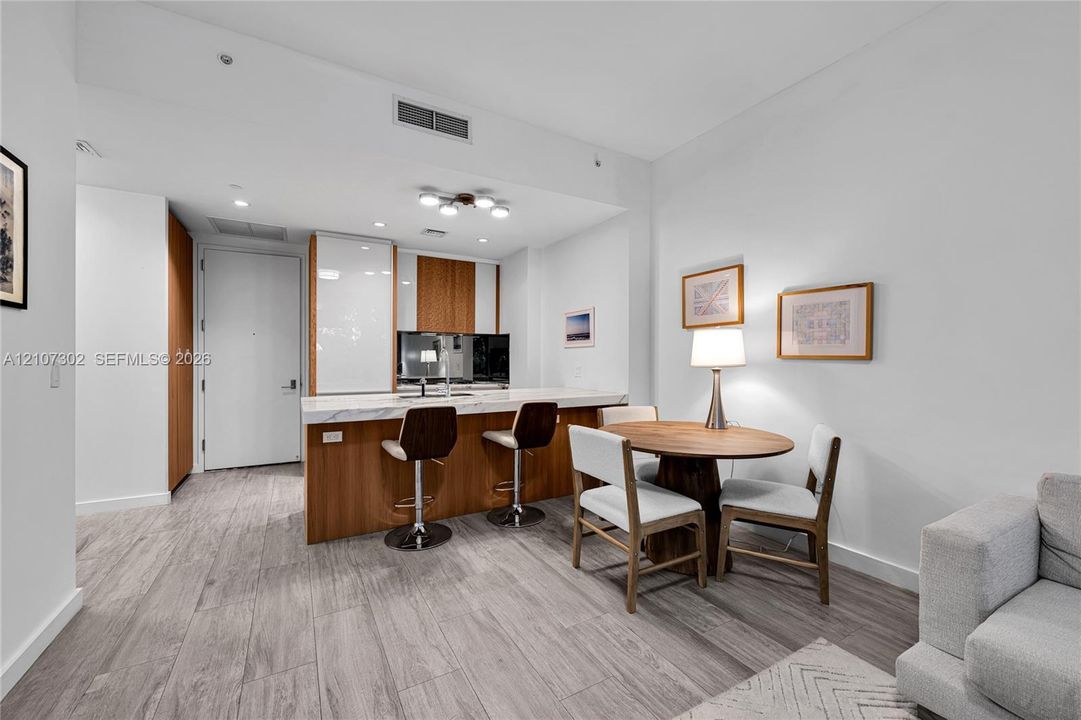 Kitchen featuring a stone-topped island with wood-finish cabinetry, floor-to-ceiling high-gloss white pantry storage, and wood-finish flooring