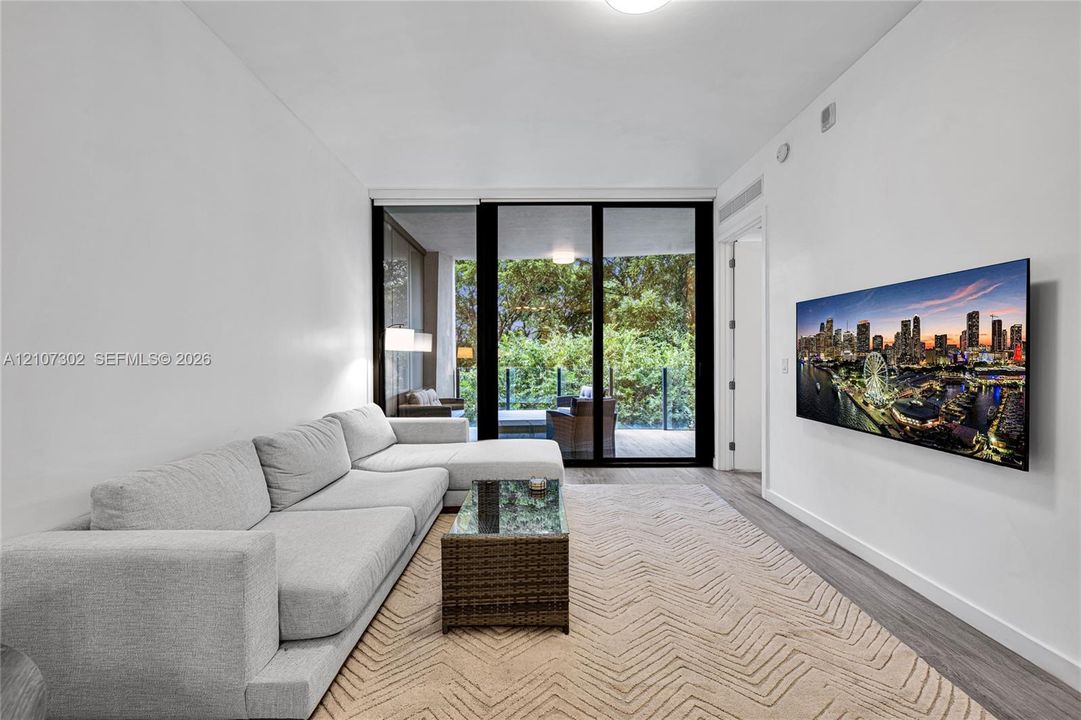 Living area featuring floor-to-ceiling glass sliding doors, wood-finish flooring, and an exterior balcony with glass railing