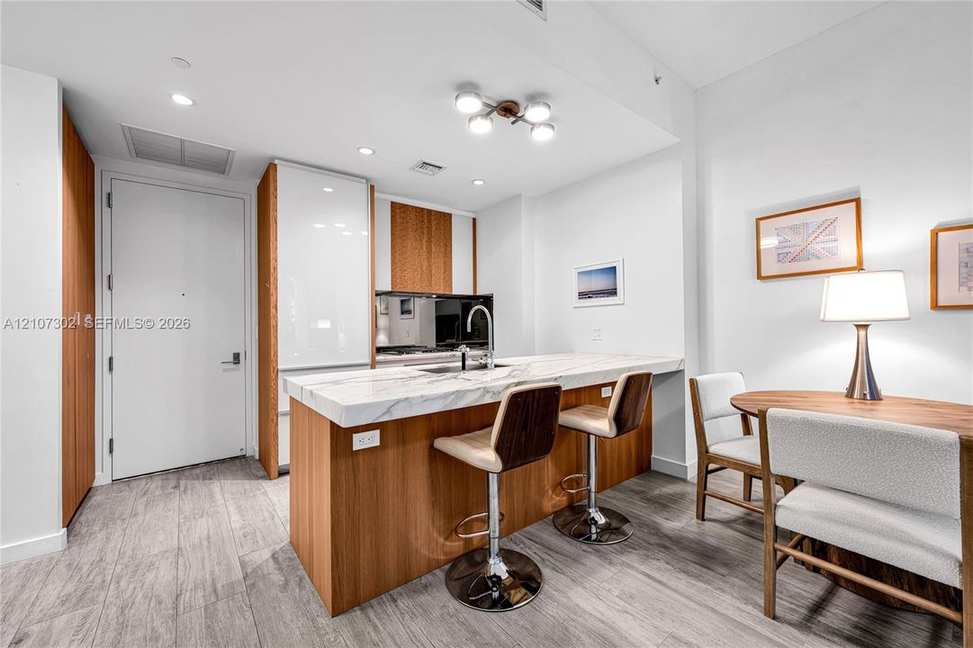 Kitchen featuring wood-finish cabinetry, white high-gloss paneling, integrated refrigerator, stone-composite countertop with waterfall edge, and wood-finish flooring