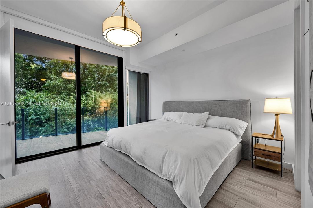 Floor-to-ceiling glass sliding doors opening to an exterior balcony, light-toned wood-finish flooring, and a circular drum pendant light fixture