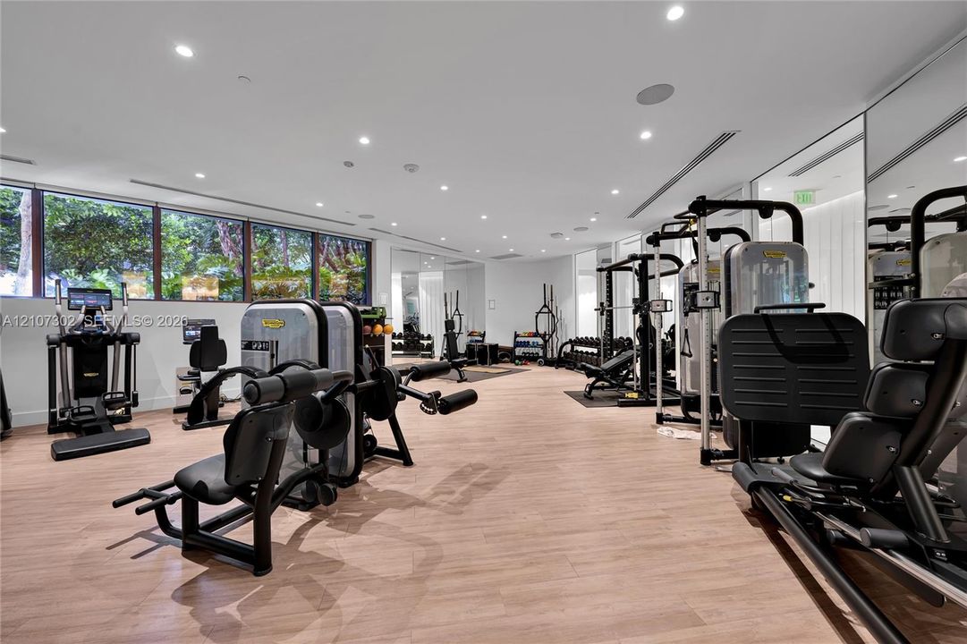 Fitness center featuring wood-finish flooring, extensive floor-to-ceiling mirrored walls, horizontal window banks, and recessed LED ceiling lighting