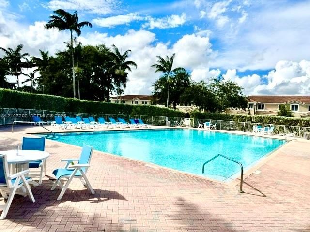 Rectangular swimming pool featuring a brick-paver deck, metal perimeter fencing, and mature landscaping