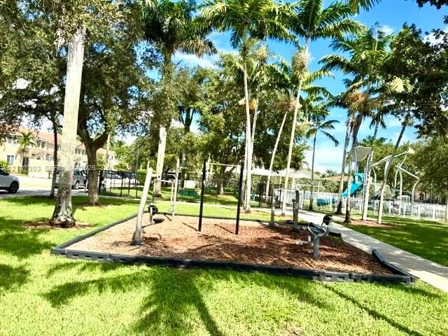 Outdoor exercise station featuring metal fitness equipment on a mulch base, surrounded by mature palm trees and manicured lawn