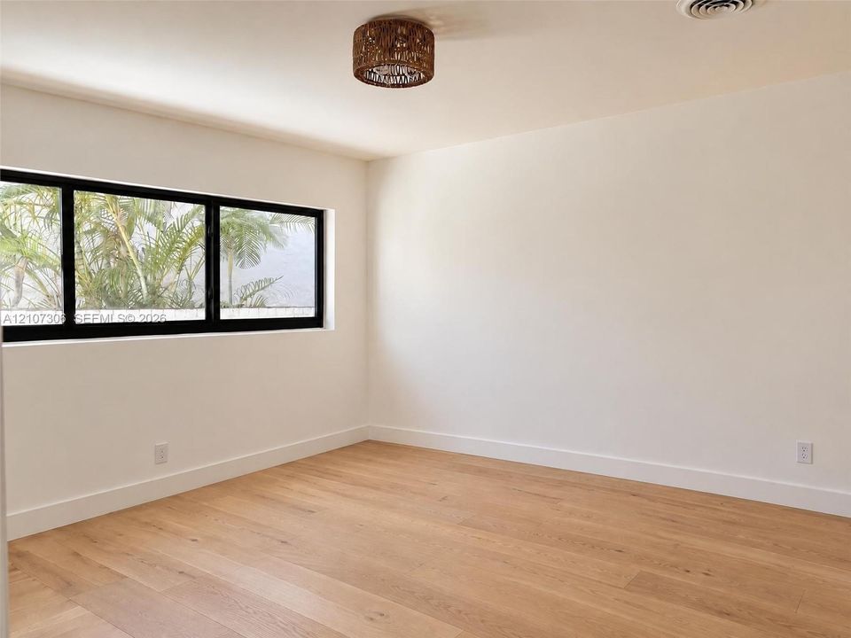 Neutral-toned interior featuring wood-finish flooring, a black-frame rectangular window, and a woven-textured flush-mount ceiling light