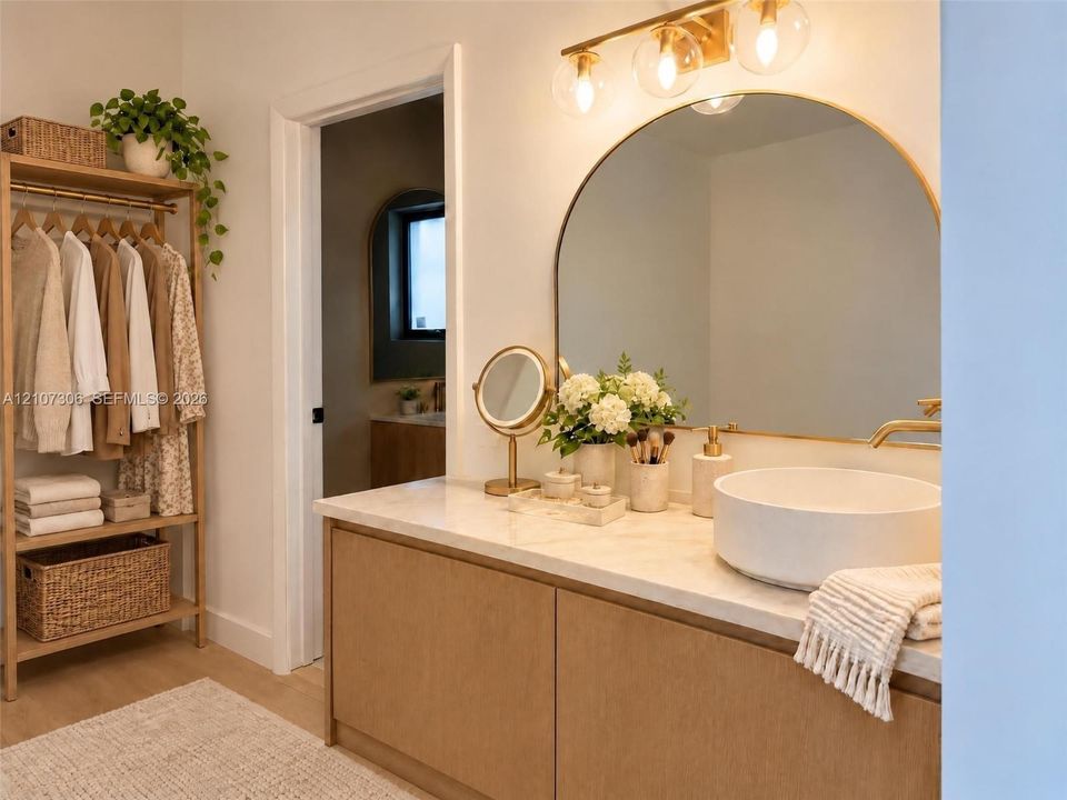 Custom wood-finish vanity with a neutral stone countertop, white vessel sink, arched wall mirror, and integrated gold-toned vanity lighting