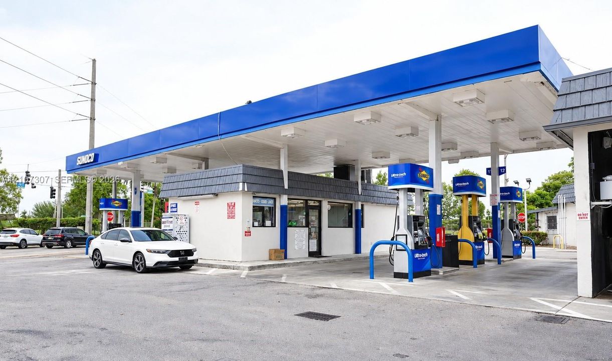 Commercial refueling station featuring a multi-pump canopy with integrated lighting, concrete forecourt, and a central service kiosk with tile-accented roof