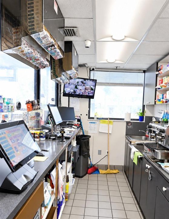 Service station workspace featuring industrial-grade metal counters, built-in dark cabinetry, a multi-basin stainless steel sink, and light-tone ceramic floor tiling