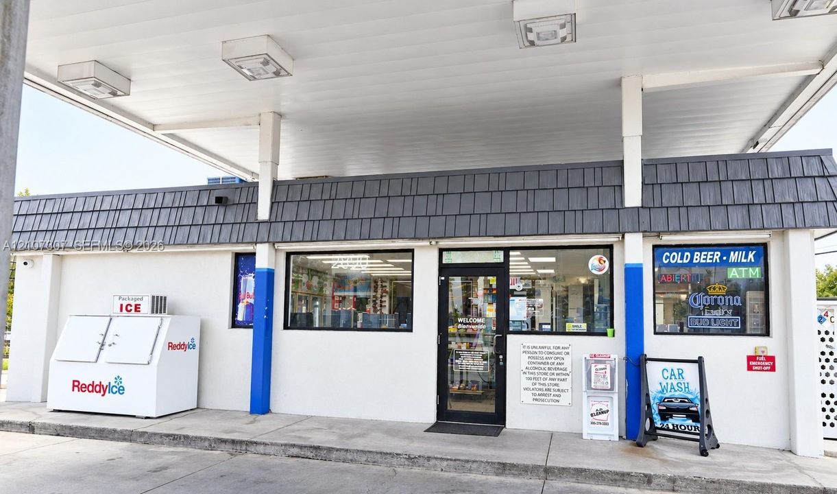 Commercial storefront featuring a covered fuel canopy, shingled mansard roofline, and concrete exterior finish