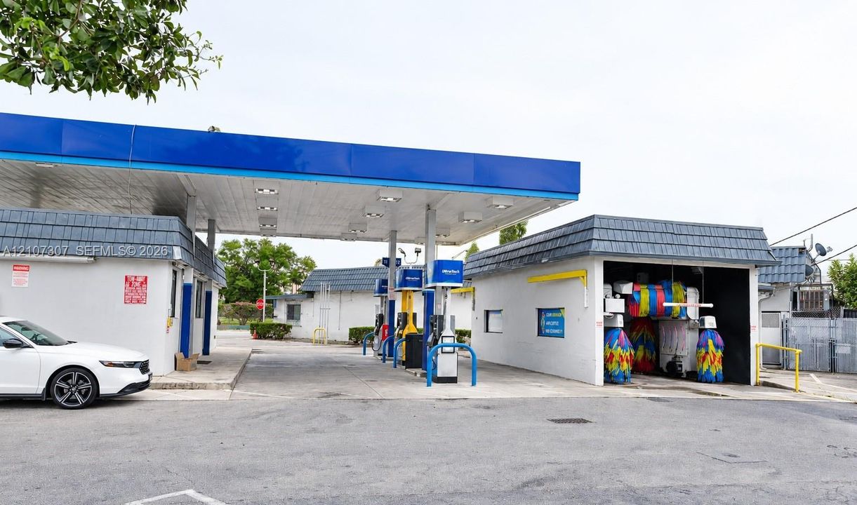 Commercial fuel station facility featuring a multi-pump canopy, integrated automated car wash bay, paved drive lanes, and masonry construction