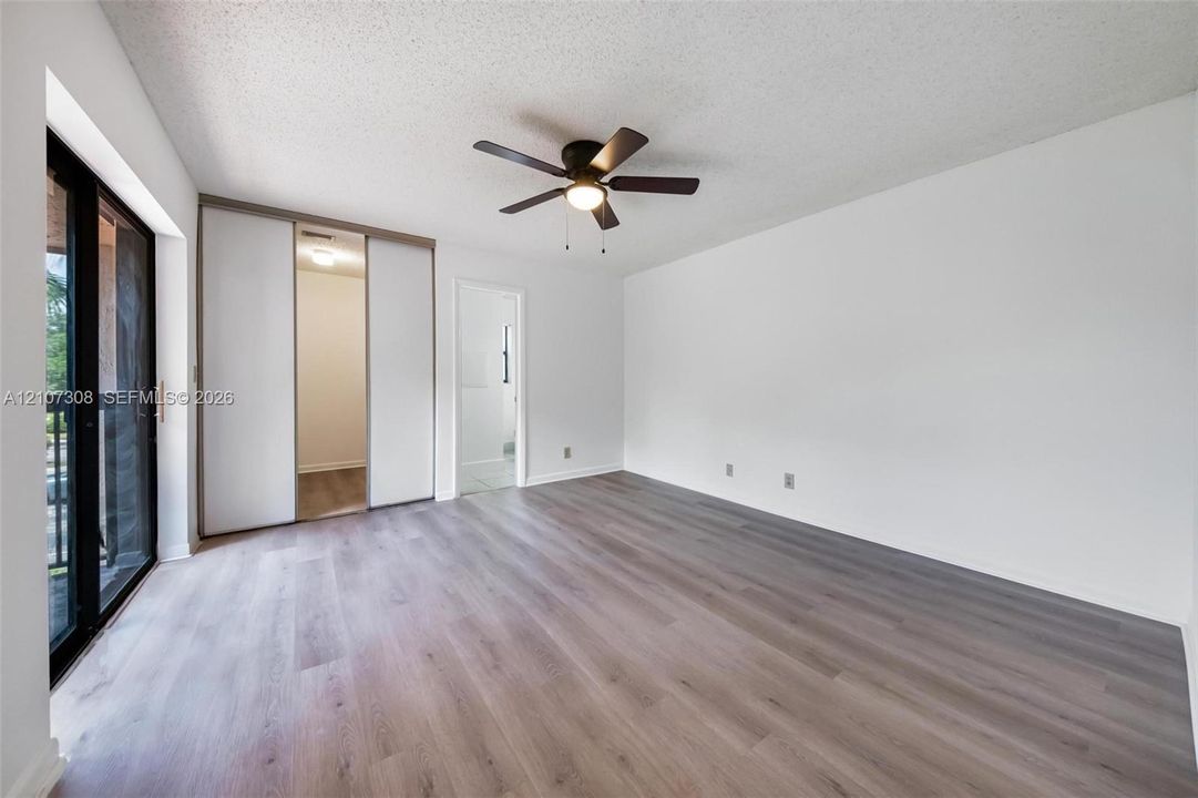 Wood-finish flooring, sliding glass patio door, built-in dual-panel closet, and overhead ceiling fan with integrated lighting